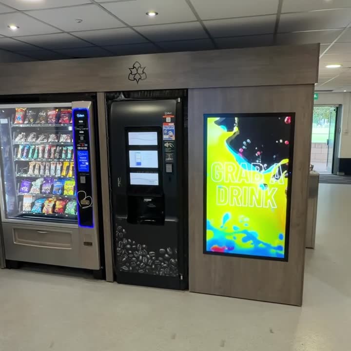 A Naxca Media screen showing a 'Grab a drink' campaign on a vending kiosk, next to a snack machine and coffee machine